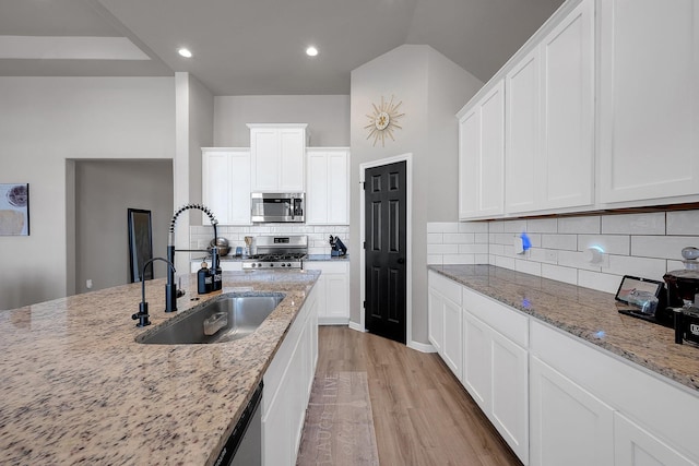 kitchen with white cabinets, appliances with stainless steel finishes, light stone countertops, light wood-type flooring, and a sink