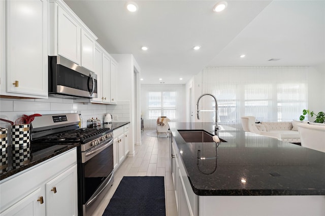 kitchen with tasteful backsplash, appliances with stainless steel finishes, white cabinetry, a sink, and an island with sink