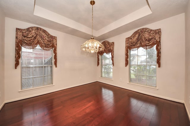 unfurnished room with a notable chandelier, a raised ceiling, hardwood / wood-style flooring, and baseboards