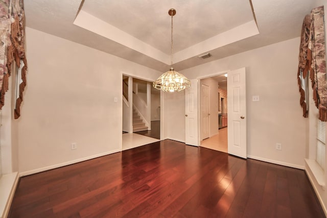 unfurnished room with baseboards, visible vents, a raised ceiling, hardwood / wood-style floors, and an inviting chandelier