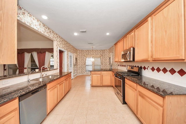 kitchen featuring wallpapered walls, appliances with stainless steel finishes, a peninsula, light brown cabinets, and a sink