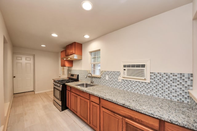 kitchen with decorative backsplash, light stone counters, stainless steel gas range, under cabinet range hood, and a sink