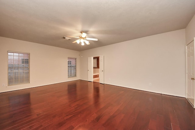 empty room featuring dark wood-style flooring, visible vents, and ceiling fan