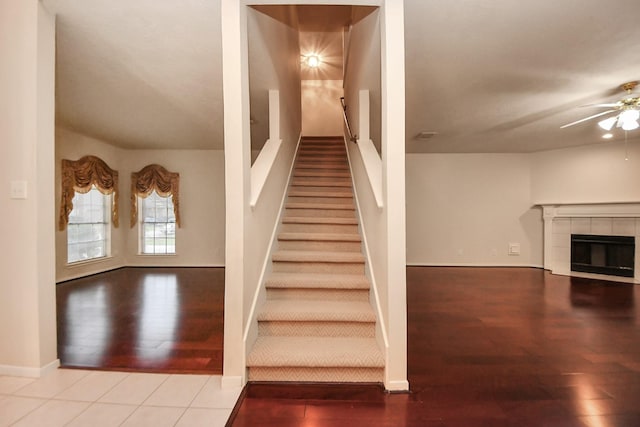 stairs featuring ceiling fan, wood finished floors, a tile fireplace, and baseboards