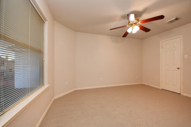 empty room featuring a ceiling fan, light colored carpet, visible vents, and baseboards