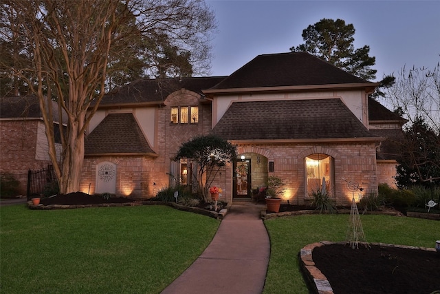 french country inspired facade with roof with shingles, a front lawn, and brick siding