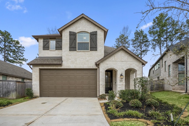 french country inspired facade featuring a garage, driveway, brick siding, and fence