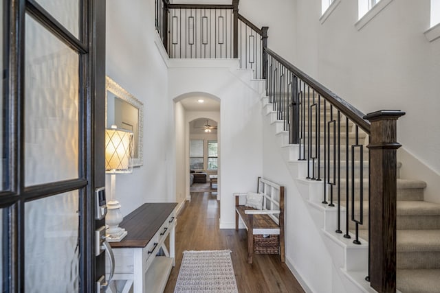 entrance foyer featuring arched walkways, ceiling fan, wood finished floors, a towering ceiling, and baseboards