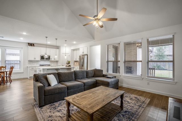 living room with ceiling fan, high vaulted ceiling, wood finished floors, and baseboards