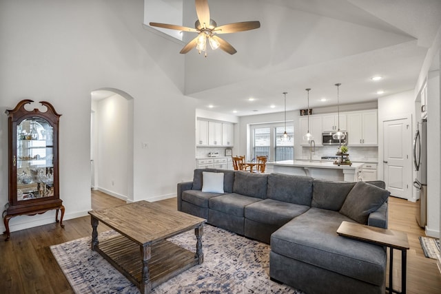 living area featuring arched walkways, a towering ceiling, ceiling fan, wood finished floors, and baseboards