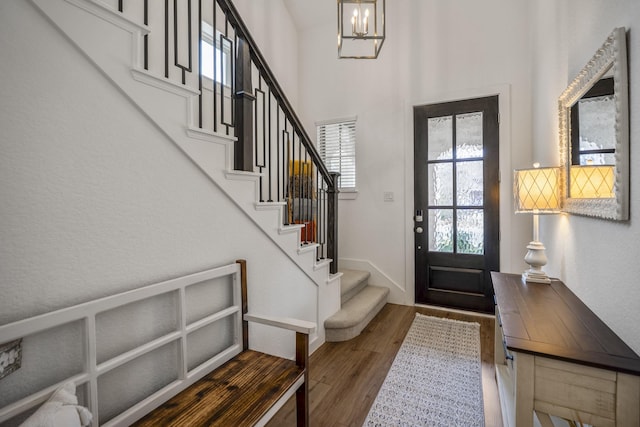 foyer entrance with a towering ceiling, an inviting chandelier, stairway, and wood finished floors