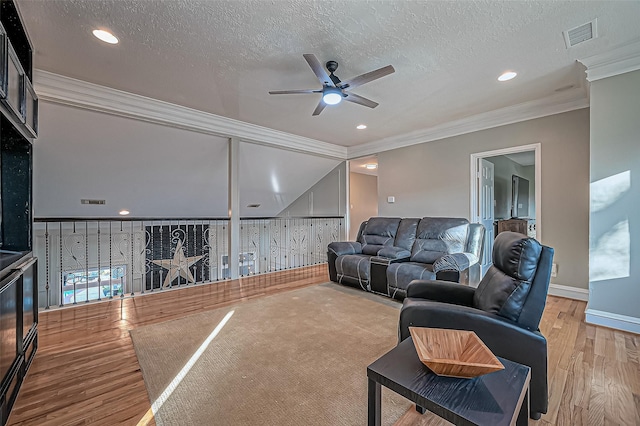 living room with a textured ceiling, wood finished floors, visible vents, baseboards, and ornamental molding