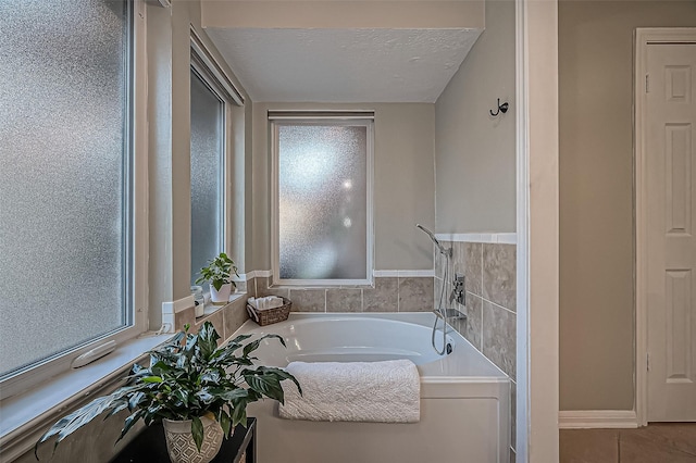 bathroom with a textured ceiling, a wealth of natural light, a bath, and tile patterned floors