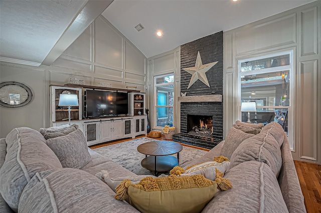 living area featuring visible vents, wood finished floors, a brick fireplace, high vaulted ceiling, and a decorative wall