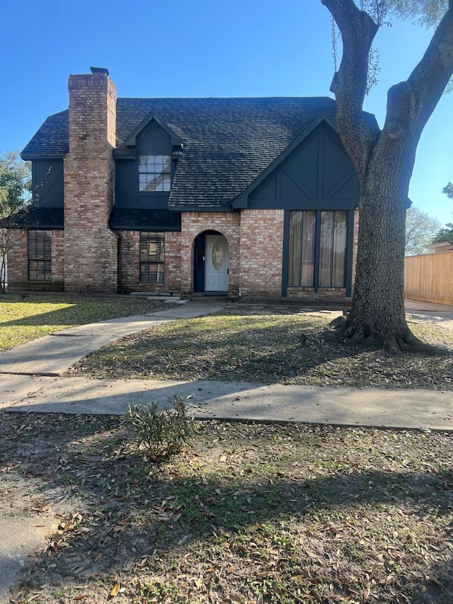 view of front facade with brick siding, a chimney, a shingled roof, and fence