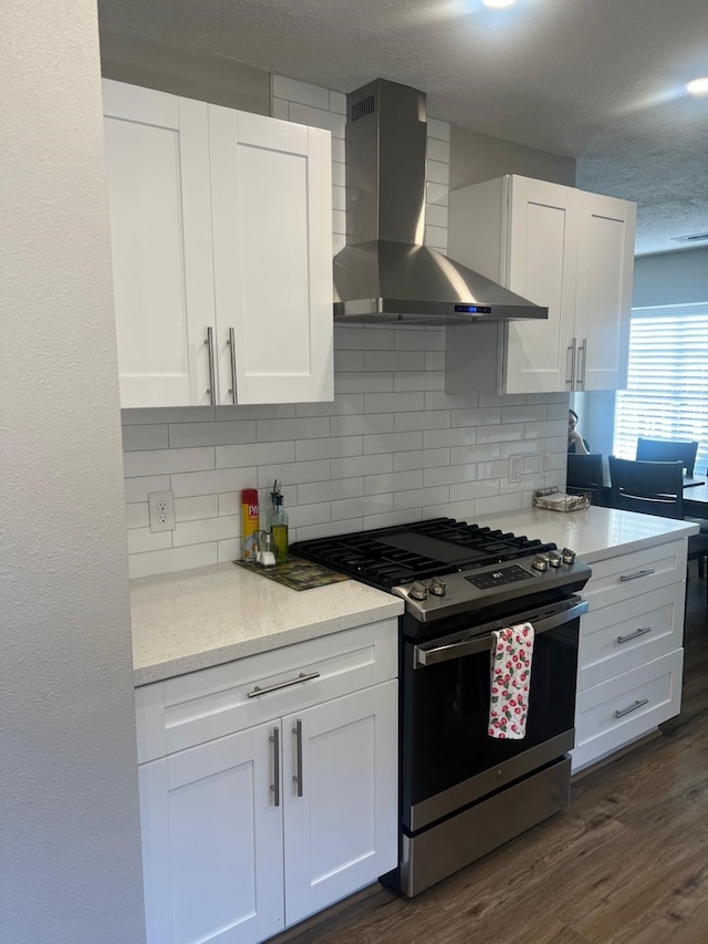 kitchen with dark wood finished floors, tasteful backsplash, stainless steel gas stove, white cabinetry, and wall chimney exhaust hood