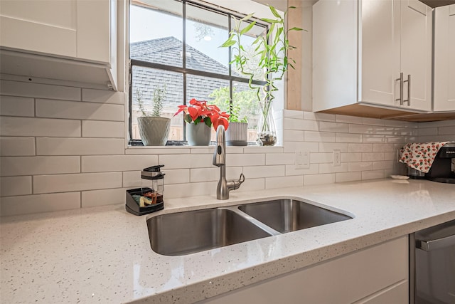 kitchen with a sink, light stone countertops, decorative backsplash, white cabinets, and stainless steel dishwasher