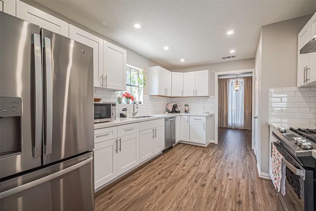 kitchen with visible vents, light wood-style flooring, a sink, stainless steel appliances, and white cabinets