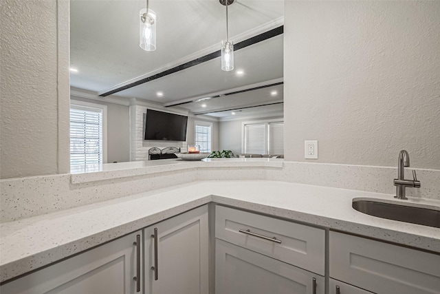 kitchen featuring light stone counters, pendant lighting, a textured wall, and a sink