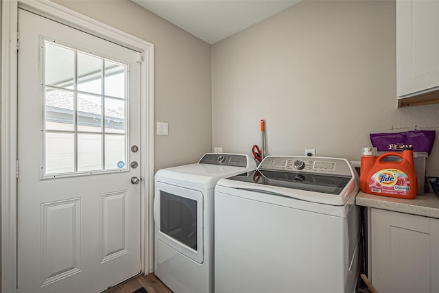 clothes washing area with cabinet space, wood finished floors, and washing machine and dryer