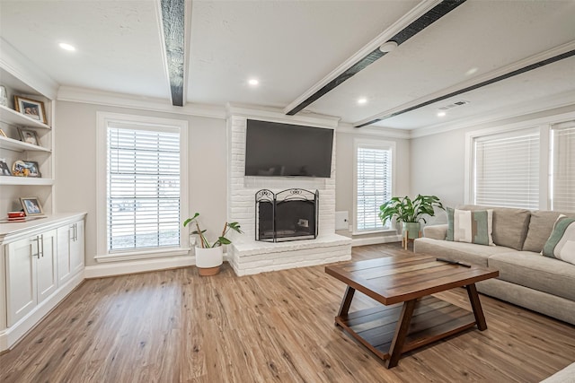 living area with light wood-type flooring, beamed ceiling, visible vents, a fireplace, and crown molding