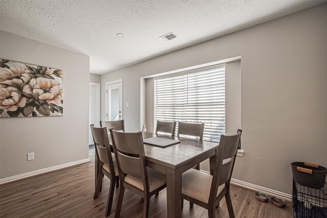 dining space featuring a textured ceiling, wood finished floors, visible vents, and baseboards