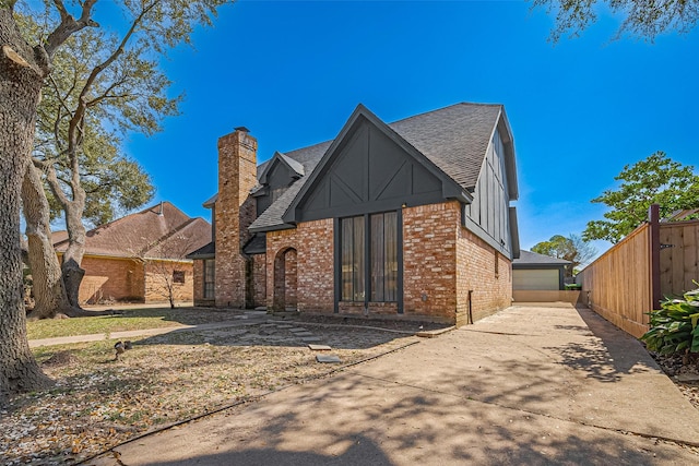 view of front of property featuring brick siding, roof with shingles, a chimney, and fence