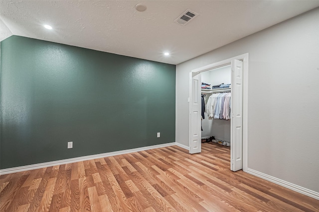 unfurnished bedroom with baseboards, visible vents, light wood-style flooring, a spacious closet, and a textured ceiling