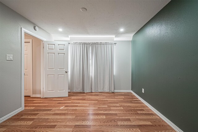empty room with recessed lighting, a textured ceiling, light wood-type flooring, and baseboards