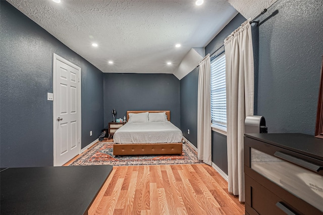 bedroom featuring baseboards, wood finished floors, vaulted ceiling, a textured wall, and a textured ceiling