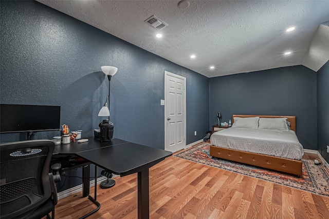 bedroom featuring vaulted ceiling, a textured ceiling, visible vents, and wood finished floors