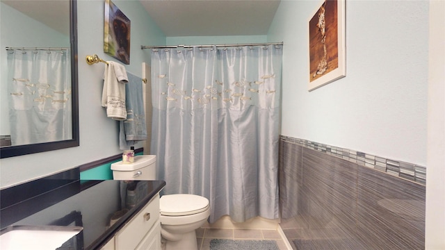 full bath featuring toilet, tile walls, vanity, wainscoting, and tile patterned floors