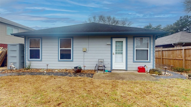 rear view of house with roof with shingles, fence, and a yard