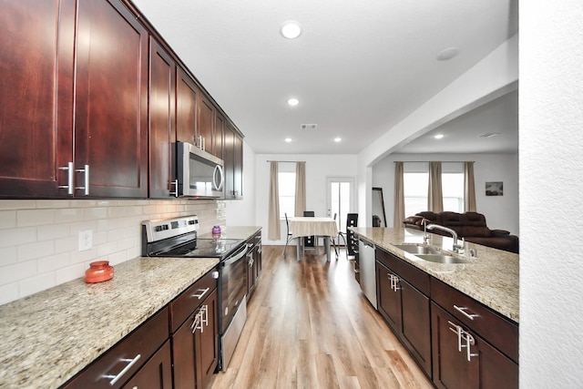 kitchen with a sink, stainless steel appliances, light wood-style floors, tasteful backsplash, and reddish brown cabinets