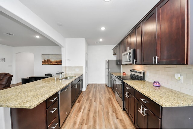 kitchen with light wood-type flooring, light stone counters, a peninsula, stainless steel appliances, and a sink