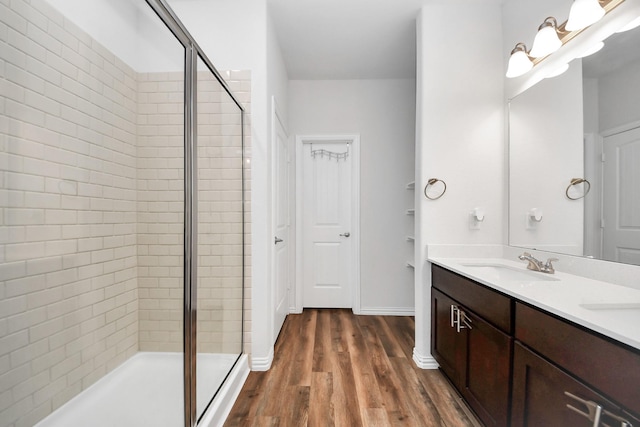 bathroom featuring wood finished floors, baseboards, double vanity, a stall shower, and a sink