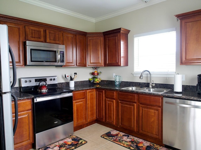 kitchen with light tile patterned floors, ornamental molding, dark stone countertops, stainless steel appliances, and a sink