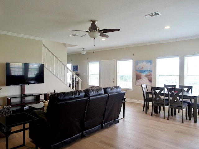 living room featuring light wood-style floors, visible vents, ornamental molding, and stairs