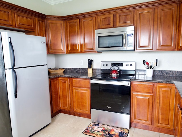 kitchen with appliances with stainless steel finishes, dark stone counters, brown cabinets, and light tile patterned floors