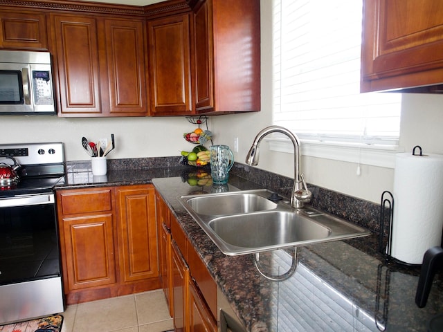 kitchen featuring light tile patterned floors, appliances with stainless steel finishes, dark stone counters, and a sink