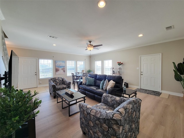 living room with light wood-style flooring, visible vents, baseboards, and crown molding