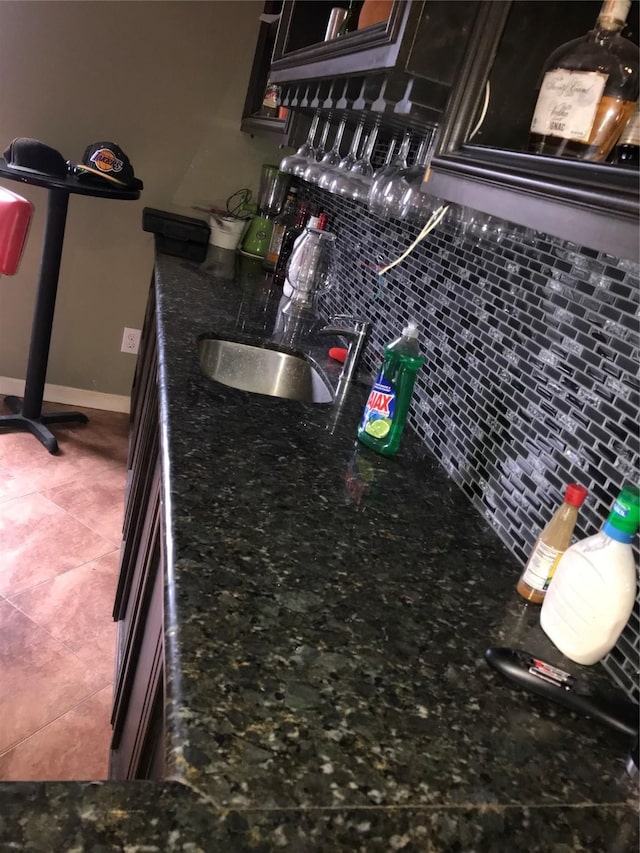 kitchen featuring decorative backsplash, a sink, dark stone counters, baseboards, and tile patterned floors