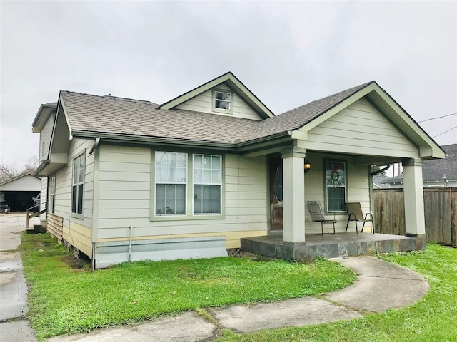 view of front of house with a shingled roof, fence, a porch, and a front lawn