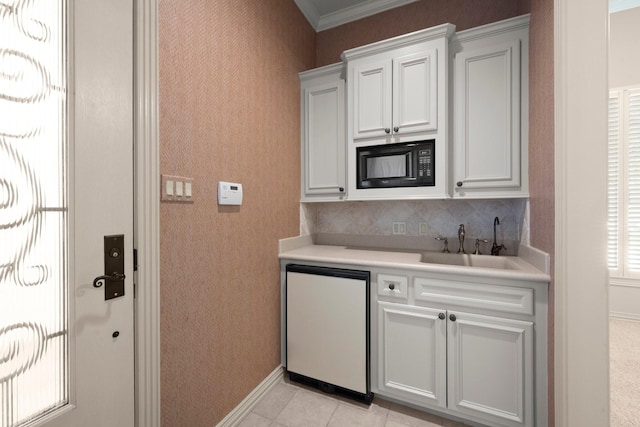 kitchen with a sink, light countertops, crown molding, black microwave, and fridge