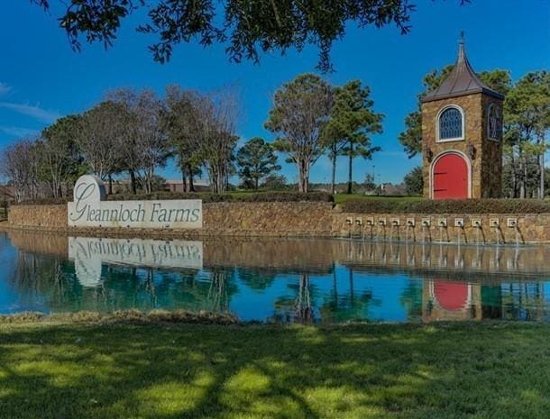 community / neighborhood sign featuring a lawn and a water view