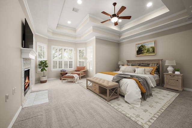 carpeted bedroom featuring a tray ceiling, a fireplace with flush hearth, and ornamental molding