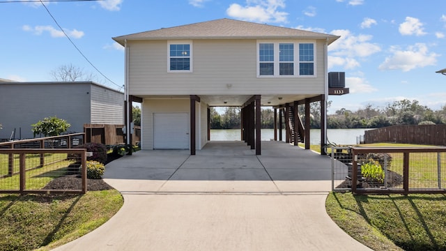 raised beach house featuring concrete driveway, stairway, a water view, a front lawn, and a carport