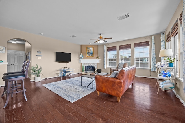 living room with arched walkways, wood finished floors, visible vents, baseboards, and a tiled fireplace