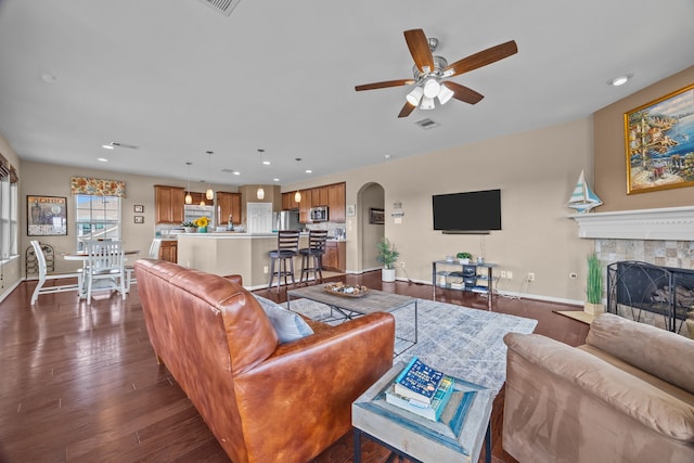 living room featuring arched walkways, a tile fireplace, visible vents, baseboards, and dark wood-style floors