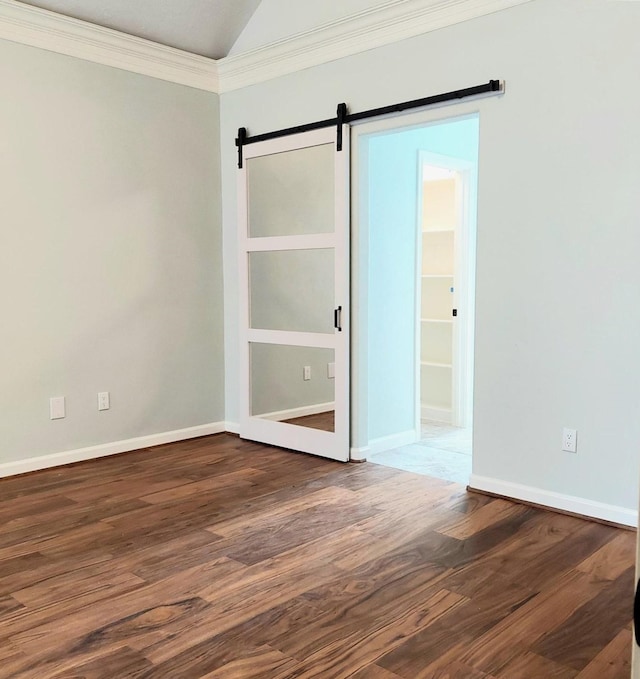 spare room with crown molding, baseboards, lofted ceiling, a barn door, and wood finished floors